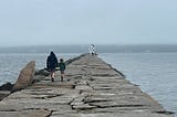 A man and his daughter hold hands and walk along a boardwalk in Maine.