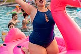 lady in swimsuit on inflatable pink flamingo with her arms in the air