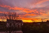 a methodist chapel behind a bare winter tree and above that is a vivid sunrise full of purple, orange and a streak of yellow