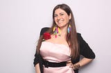 The author, me, dressed in a smart outfit composed of a satin baby pink dress and a black vest complimented with  multicolored feather earrings.