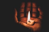 Hand holding lit candle stub in their palm.