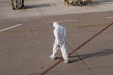 A tired looking person in a full-body protective suit, symbolizing the intersection of public health and safety.
