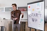 Young man giving a pitch with a blackboard that reads “startup”