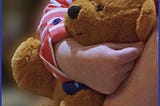 The arm of a toddler wrapped around a brown Teddy bear