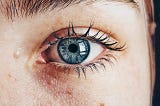 A close-up of a woman’s blue eye and imperfect skin.