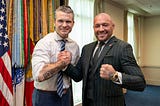 Pete Hegseth in a shirt and tie with one sleeve rolled up showing a We The People tattoo. He has locked fists in a friendly way with Conor McGregor, who is wearing a suit, tie and jacket, showing a gold watch.
