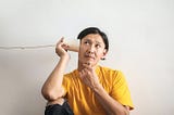 Man trying to listen to something with a paper cup and string