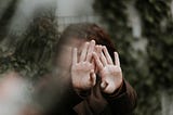 A young woman has her hands outstretched in front of her face, with her palms facing forward. The image focuses on her palms while the rest is blurred.