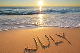 A beach, the sea and “July” written on the sand