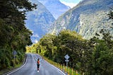 Lady walking along a road which cuts through bush clad mountains.