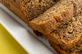 Gluten free banana bread, with 3 slices cut sitting on a white plate. bright yellow brackground.