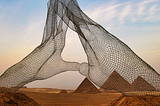 A silhouette of hands in a mudra gesture, resembling a massive wire statue towering over the pyramids in the desert.