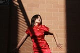 The author, a Chinese American woman, in a cheongsam against a brick wall. The photo style is fashion/editorial.