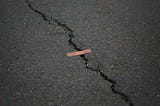 A jagged crack in the road with a Band Aid crossing it.