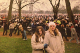 Huge crowd of people in Hyde Park, amongst trees and grass. Young India and her Mum stand in front looking at camera.