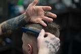 Photo of a young man getting a haircut by a tattooed barber.
