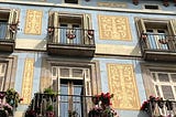 An ornate apartment building facade with flowers on the balconies and colorful wall designs.