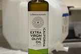 A bottle of olive oil in front of a jug of bottled water at the sink.