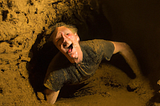 DALL-E generated image shows a person “having fun” in a cave — squeezeing through a small gap surrounded by mud.