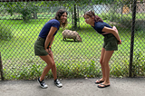 Mom and daughter wearing matching navy blue tops and forest green shorts posing with a capybara behind the fence