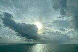 open ocean, clouds backlit by sun, light on water, greys, blues