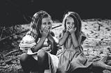 Black and white photograph of two little girls laughing while covering their mouths.