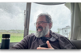 The author smiles while sitting inside an Airstream on a rainy day, holding a phone during a recording.