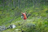 A blonde woman in a red dress dancing in nature.