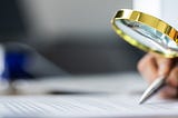 Auditor Doing Tax Fraud Investigation, a woman’s hand with a magnifying glass and papers on a table