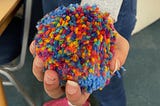 A hand holding a multicoloured pom-pom
