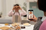 Happy european adult woman taking photo on smartphone screen of little girl in apron, making cookie