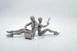 Two grey human-like figures, presumably bots, sit on the ground. One is using a laptop and the other is looking at a tablet.