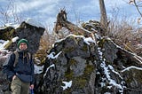 WWU Geology graduate student Brendan Garvey stands in front of a snow-dusted rock formation.