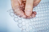 Hand popping a piece of bubble wrap.