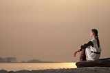 Woman sitting by ocean on a rock looking over the water.