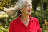 Older woman, gray hair blowing in the breeze, face and neck wrinkles, smiling in nature