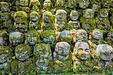 Rows of small stone statues covered in moss, set into a wooded hillside at Daikaku-ji Temple in Kyoto.