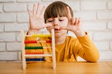 Child in yellow shirt learning how to count in front of an abacus