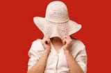 lady in off white with hat pulled over her eyes against red background