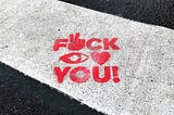 The words “Fuck you” spray painted in red on a pedestrian zebra crossing