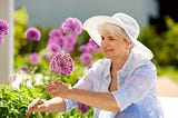 n older grey haired woman standing by purple flowers and smiling friendship death seniors