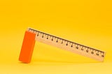 A ruler with one end leaning on an orange block with a yellow background.