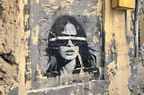 An image of a spray painted wall with a woman that has tape over her eyes