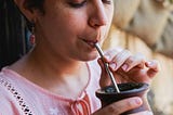 woman in pink shirt, eyes closed drinking brown mug with metal silver straw