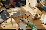 Overhead view of a person writing in a journal at a desk with a computer on it