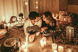 A smiling man and woman gaze into each other’s eyes in a candlelit room.