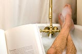 Man’s hairy legs, bubble bath, brass faucet, book