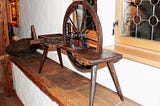 A photo of a wooden spinning wheel sitting on a shelf by a window.