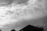 a roof and a cloudy sky in black and white