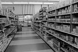 a black and white photograph of an aisle in a grocery store taken in 1976